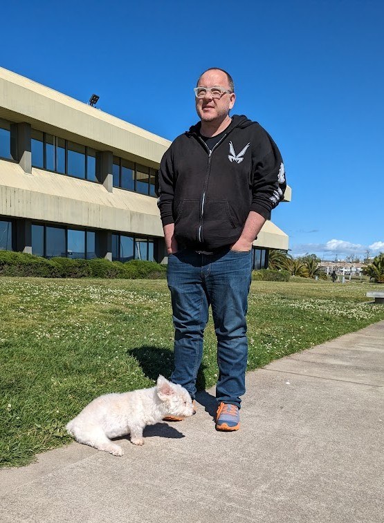 Jeff outside on a sunny day with his small white dog, Casper