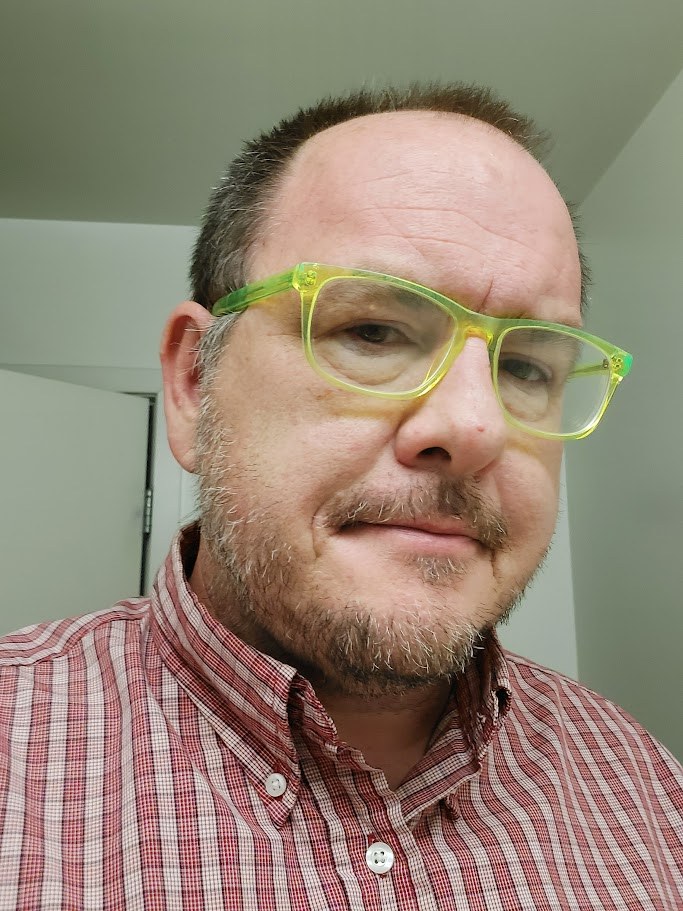 Jeff Pollet — smiling, wearing bright green glasses and a red plaid shirt